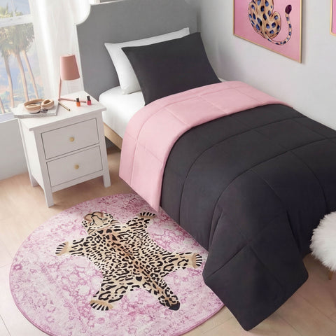 A neatly made twin bed with a black and pink comforter sits next to a white nightstand. A Finely Washable Round Rug with a cartoon leopard design and non-skid backing lies on the floor, while a framed leopard print hangs on the wall.