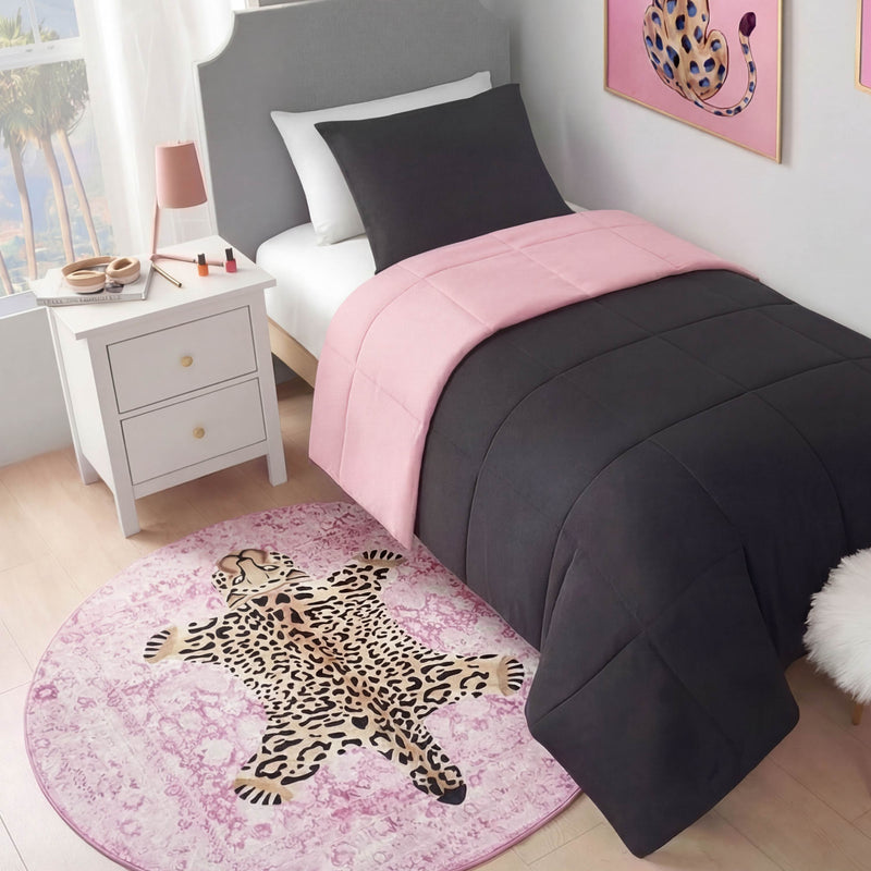 A neatly made twin bed with a black and pink comforter sits next to a white nightstand. A Finely Washable Round Rug with a cartoon leopard design and non-skid backing lies on the floor, while a framed leopard print hangs on the wall.