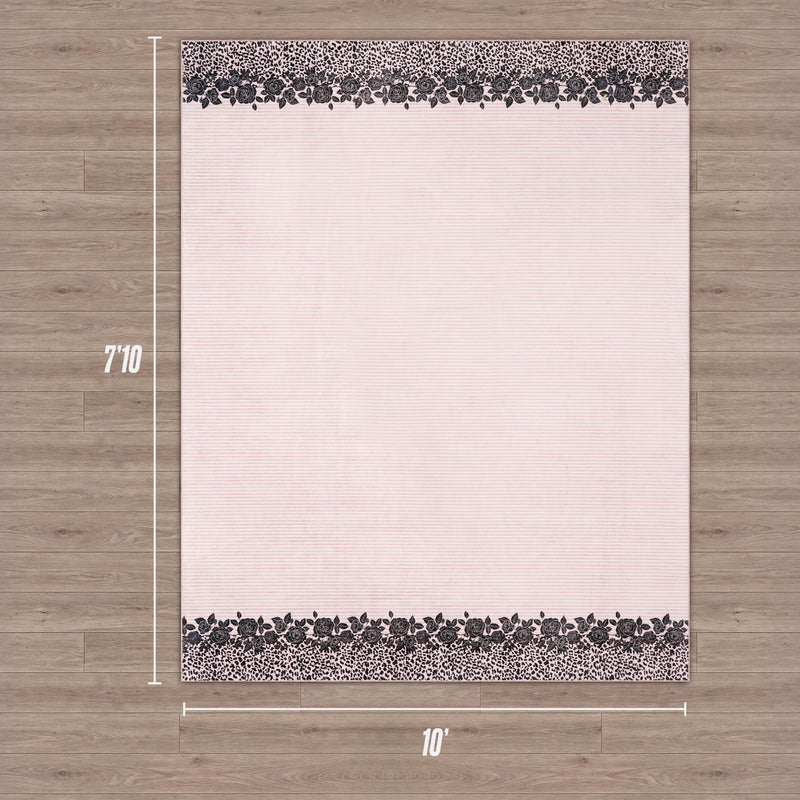 Ultra-soft, the Finely Washable Rug (7'10" x 10') has a light pink center and dark floral patterned borders on two sides, shown on a wood floor.