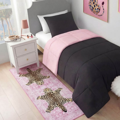 A neatly made bed with dark gray and pink bedding sits by a white nightstand with makeup. On the floor lies a Finely Washable Rug, 2' x 6', featuring two leopards, while a leopard-themed picture hangs above the bed.