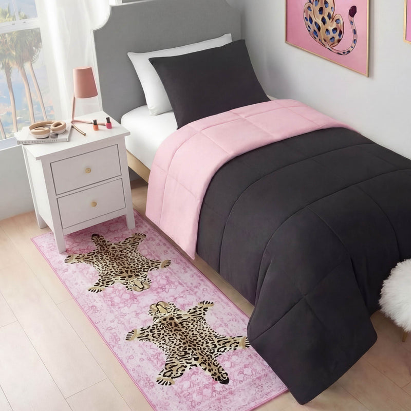 A neatly made bed with dark gray and pink bedding sits by a white nightstand with makeup. On the floor lies a Finely Washable Rug, 2' x 6', featuring two leopards, while a leopard-themed picture hangs above the bed.