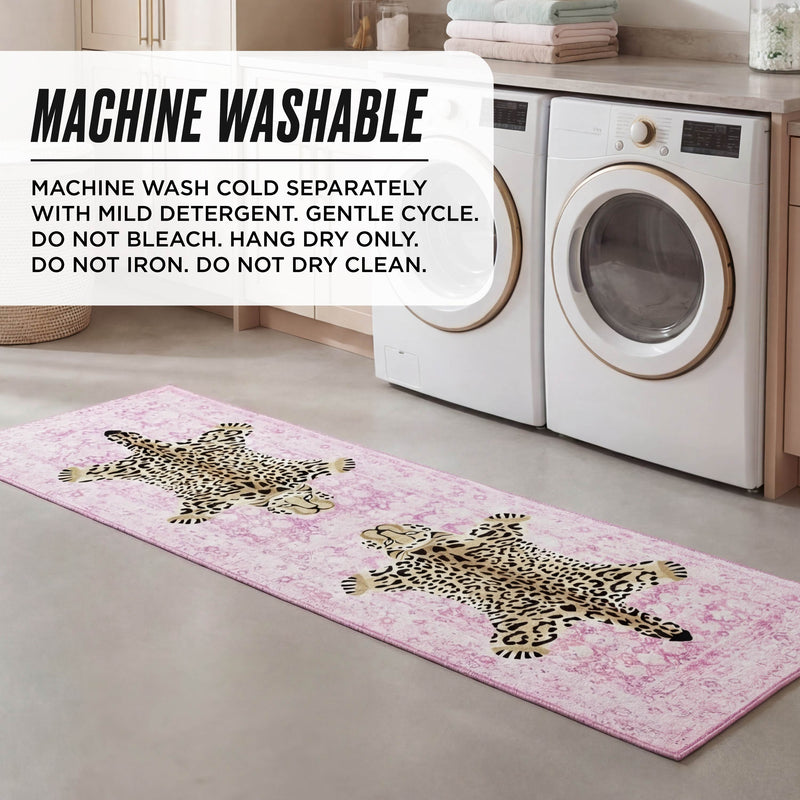 A pink Finely Washable Rug, 2' x 6', featuring two leopard designs, is placed in front of a washer and dryer in a laundry room. Machine washing instructions are shown, with cabinets and laundry baskets visible in the background.
