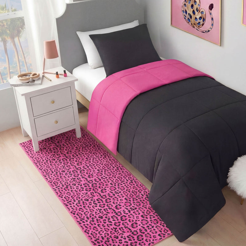 A neatly made twin bed with a dark gray comforter and bright pink accents sits beside a white nightstand. A Finely Washable Rug, 2' x 6', with pink leopard print and wall art add a bold touch to this modern room.