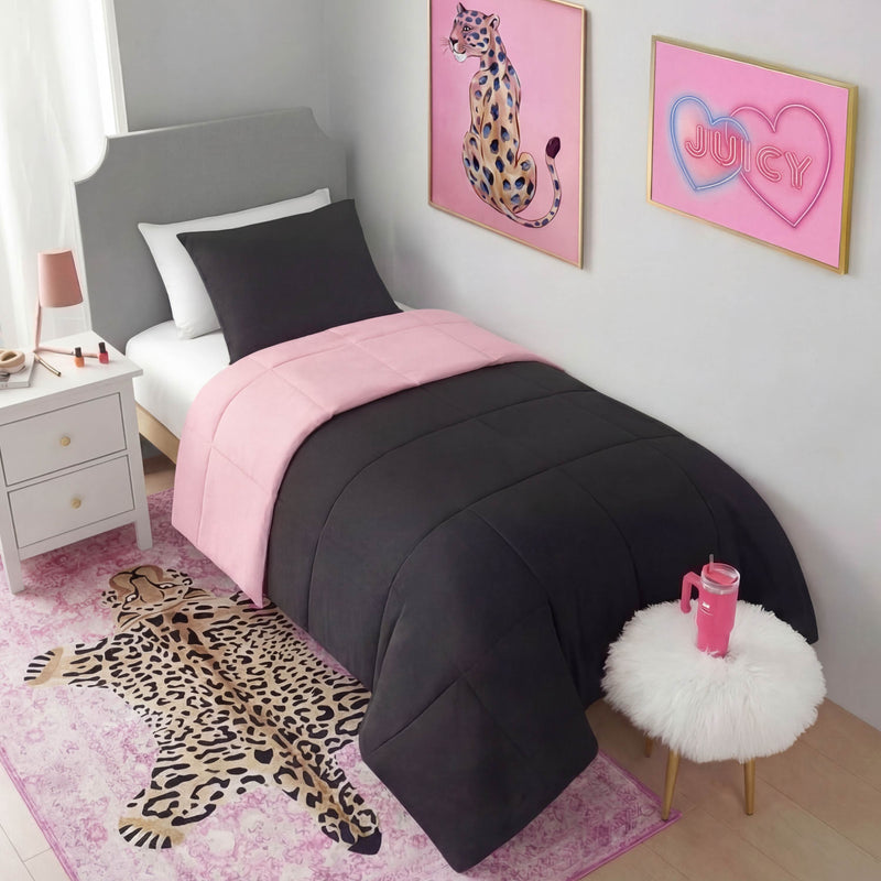 A neatly made twin bed with black and pink bedding sits beside a lamped nightstand. The room has pink leopard decor, including a Finely Washable Rug (5' x 7'), wall art, and a fuzzy stool topped with a drink tumbler.