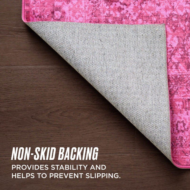 The Finely Washable Rug, 5' x 7', features a pink pattern and ultra-soft texture. One corner is lifted to reveal its gray non-skid backing on a wooden floor, providing stability and helping prevent slipping.