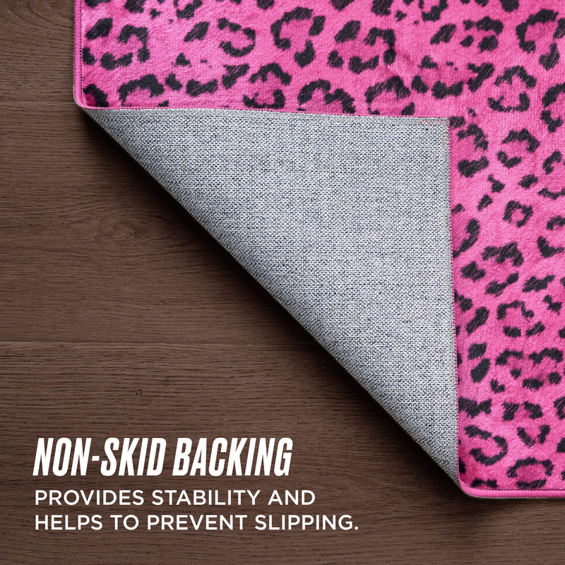 A pink leopard-print Finely Washable Rug, 5' x 7', is partially flipped to reveal its gray non-skid backing on a wood floor. Text: Non-skid backing keeps the rug stable and slip-resistant. This ultra-soft rug brings a stylish touch to any room.