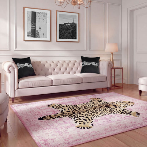 A chic living room with a tufted light pink sofa, two black leopard pillows, a Finely Washable Rug (7'10 x 10') featuring leopard print, modern wall art, a standing lamp, and light wood floors.