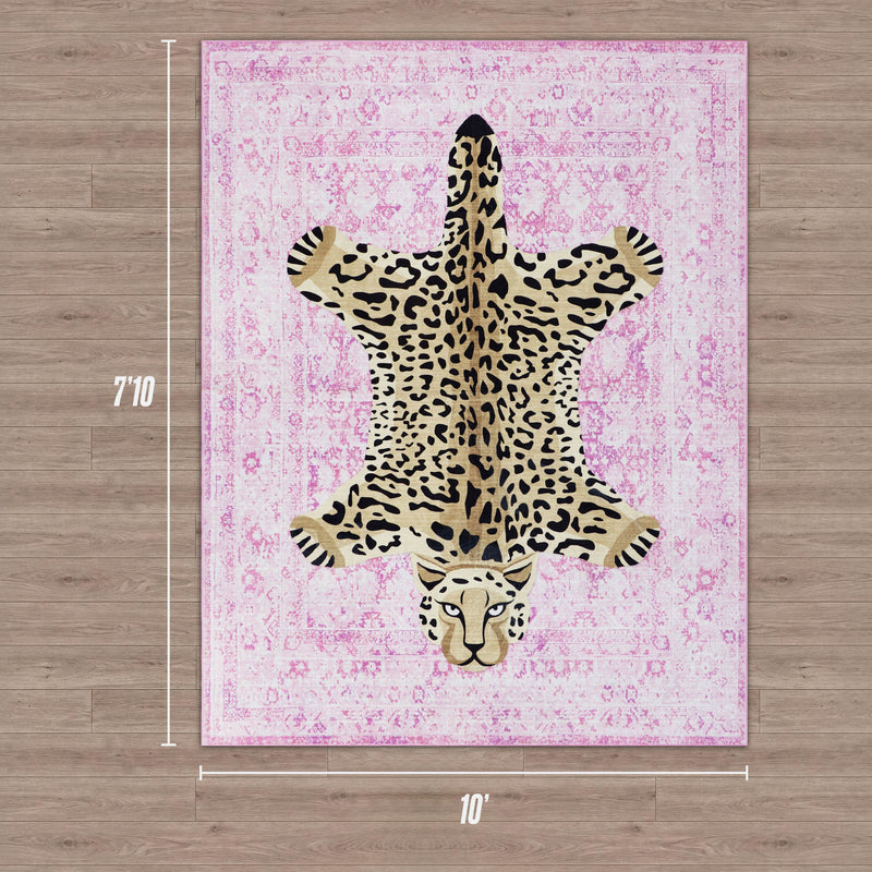 A rectangular Finely Washable Rug, 7'10 x 10', features an ultra-soft pink pattern with a bold leopard design in the center, resembling a skin rug, and is displayed on wood flooring.