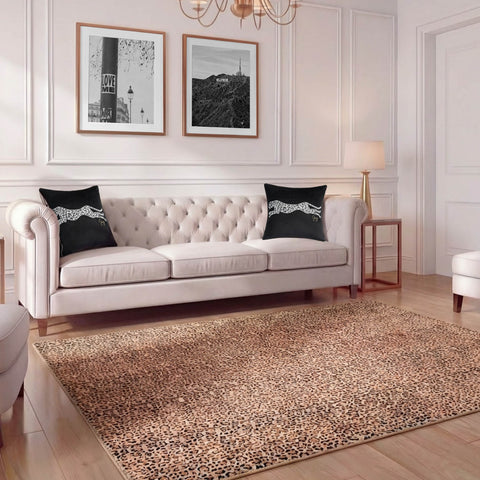 A stylish living room featuring a tufted cream sofa, two black cheetah-print pillows, the Finely Washable Rug (7'10 x 10') in leopard print, a modern lamp, framed black-and-white art, and elegant white walls with molding.