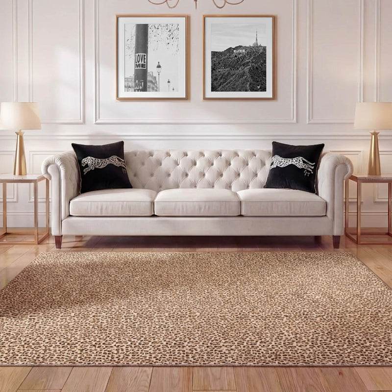A living room with a tufted beige sofa, two black pillows, a Finely Washable Rug (7'10 x 10') in leopard print, two matching lamps on side tables, and two framed black-and-white photos above the couch.