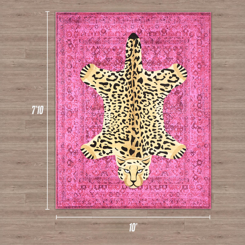 The Finely Washable Rug, 7'10" x 10', is a pink rectangular ultra-soft rug with a large leopard-skin design in the center, shown on a wooden floor.