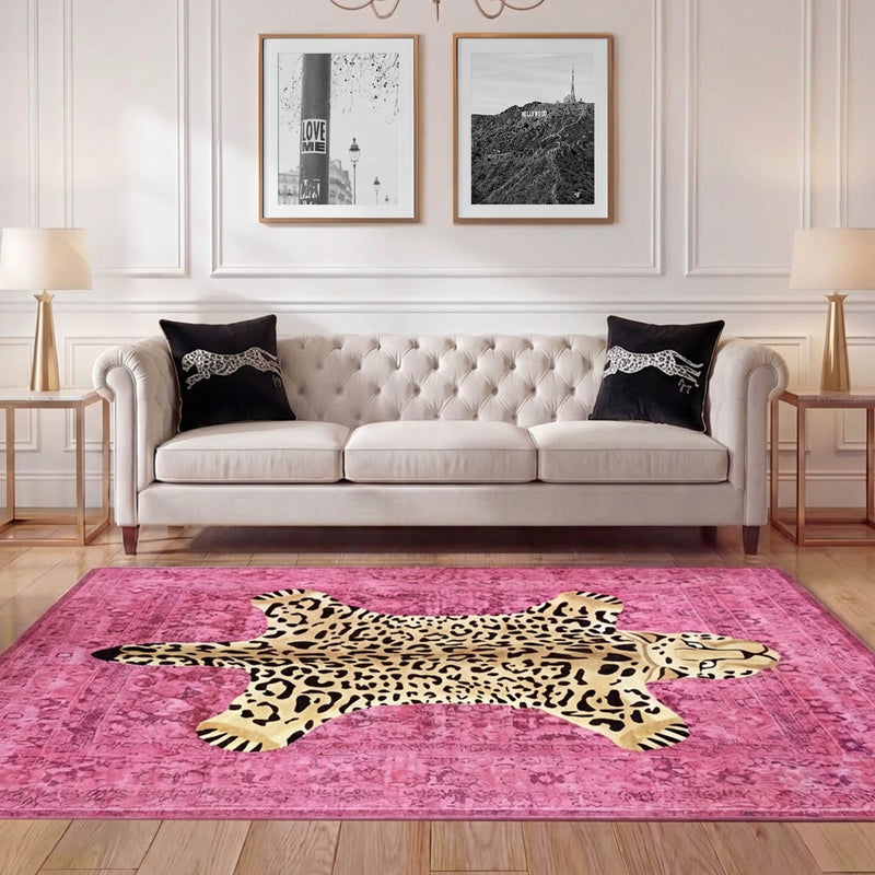 A stylish living room features a tufted beige sofa with black pillows, gold side tables, lamps, and an ultra-soft Finely Washable Rug (7'10 x 10') in pink leopard print. Three framed pictures hang on the white paneled wall behind the sofa.