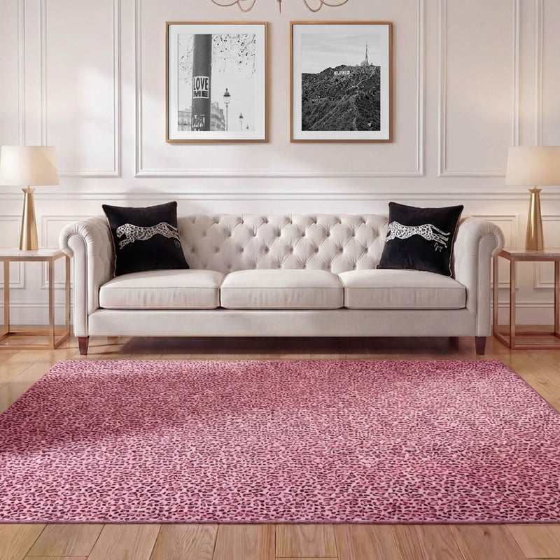 A stylish living room features a tufted cream sofa, two black pillows, gold side tables with lamps, framed wall art above, and a large pink Finely Washable Rug (7'10 x 10') with non-skid backing on a wooden floor.