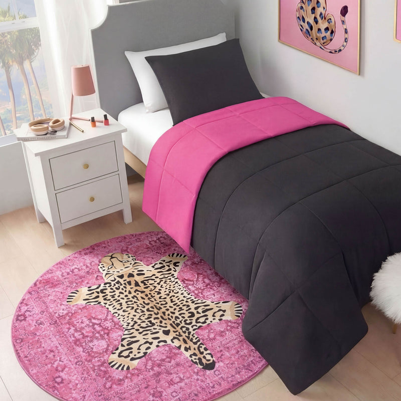 A neatly made twin bed with dark gray and bright pink bedding sits beside a white nightstand. On the floor is the Finely Washable Round Rug featuring a leopard design, complemented by leopard artwork on the wall.