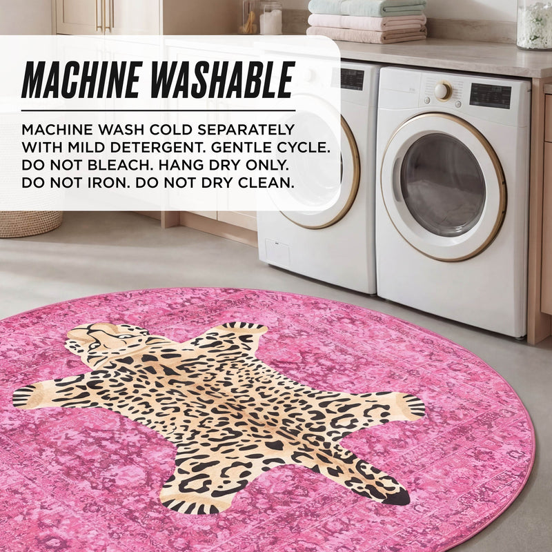 A laundry room with a front-loading washer and dryer, light cabinets, and the Finely Washable Round Rug in pink featuring a cartoon leopard design. Overlay text provides machine wash instructions for this ultra-soft, washable rug.