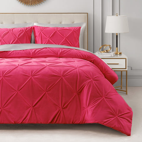 A neatly made bed with the vibrant pink Kiss Pleat Micromink Comforter Set and matching pillows sits next to a white nightstand topped with a white and gold lamp, gold rings, and a book in this modern, stylish bedroom.