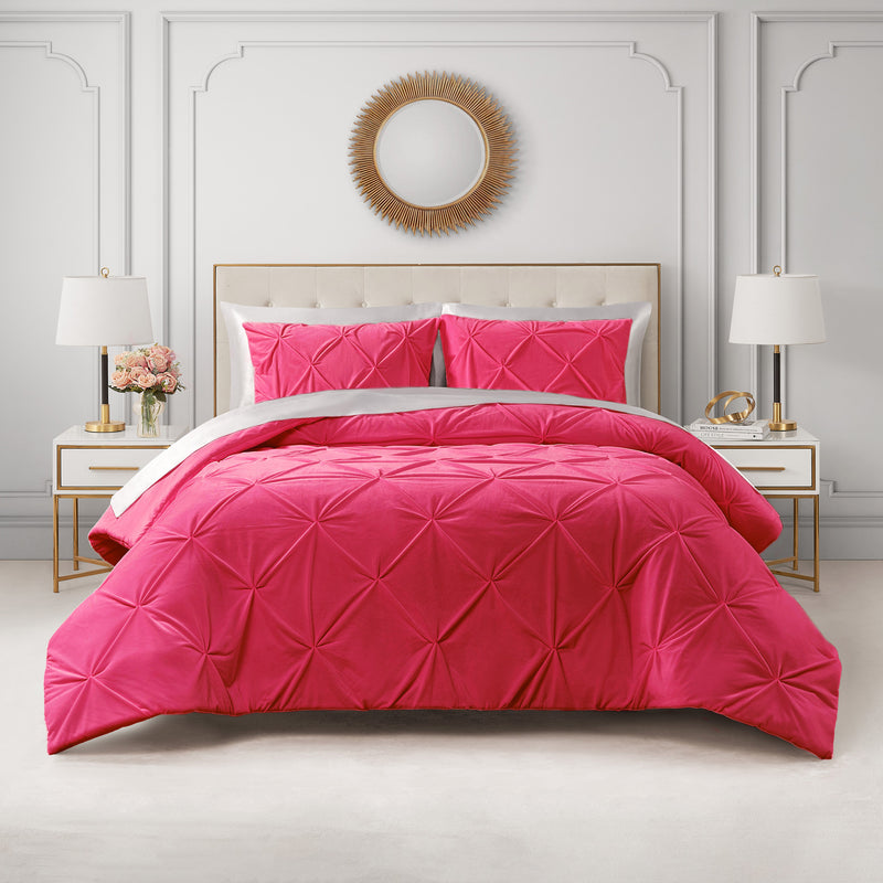 A neatly made bed with the Kiss Pleat Micromink Comforter Set in vibrant pink and matching pillows, flanked by white and gold nightstands with lamps, set against a light gray paneled wall with a round decorative mirror above.