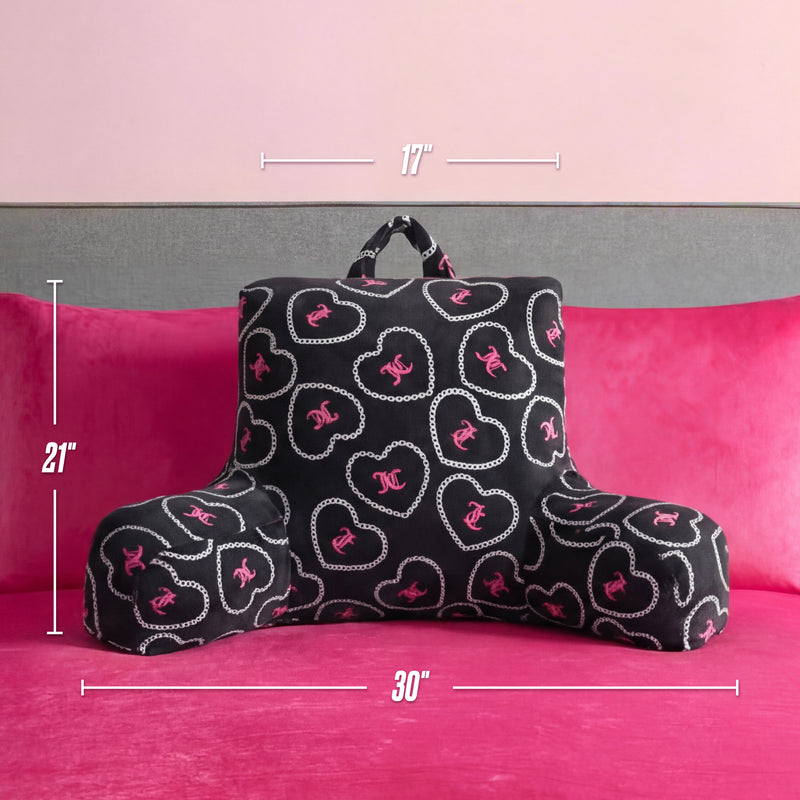 A Juicy Couture Backrest Pillow with pink and white heart and chain designs rests on a hot pink bed; this plush pillow measures 21" tall, 17" wide at the top, and 30" wide at the base.