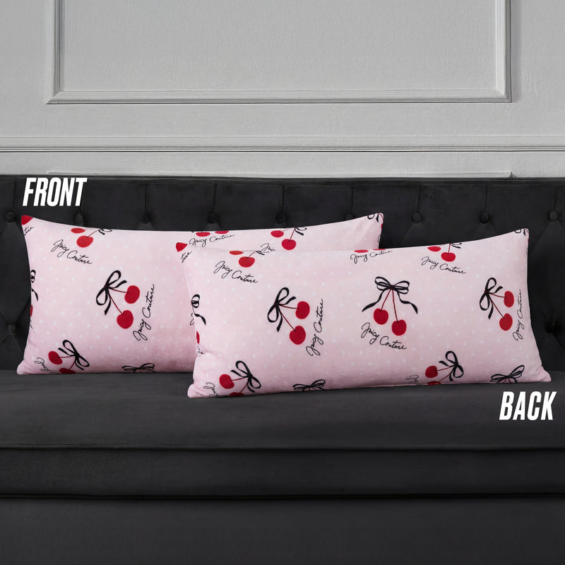 Two pink Plush Body Pillows with red cherries, black bows, and script branding add a chic touch. Labeled "FRONT" and "BACK," these oversized pillows rest on a dark gray couch.