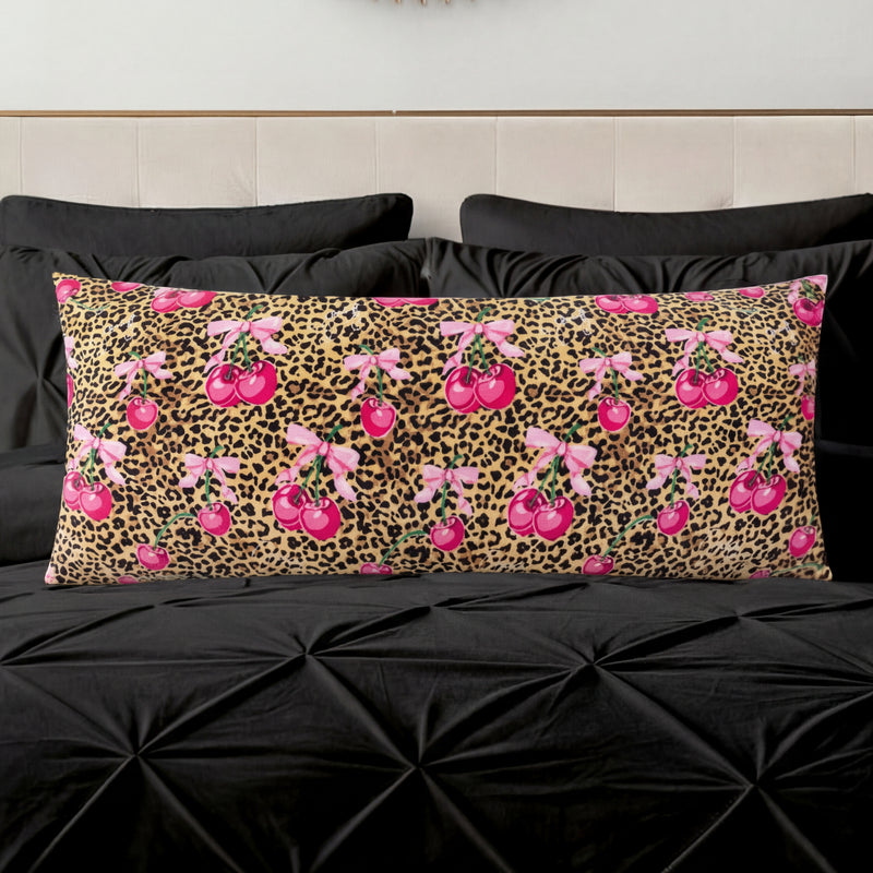 A Plush Body Pillow featuring a leopard print with bright pink cherries and pink bows, shown on black bedding and a cream-colored headboard.