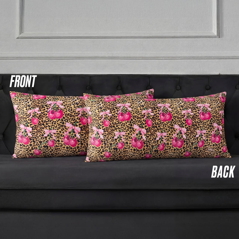 Two rectangular Plush Body Pillows on a black couch display a pink cherry and brown leopard print, reminiscent of Juicy Couture. Labels "FRONT" and "BACK" show both sides of the design.