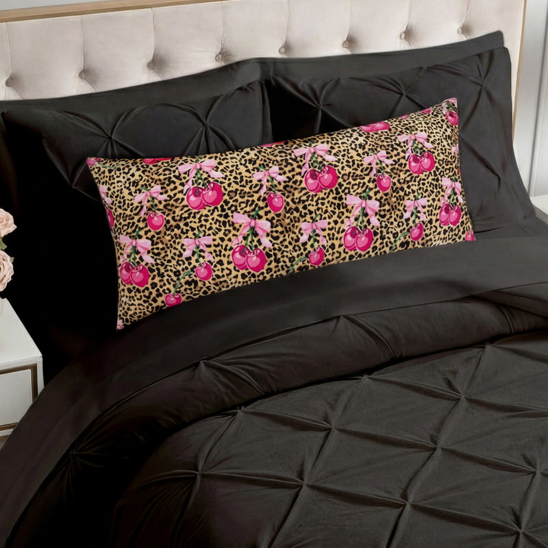A bed with black tufted bedding and a Plush Body Pillow rests before a beige tufted headboard, featuring a leopard print background with pink cherry patterns.
