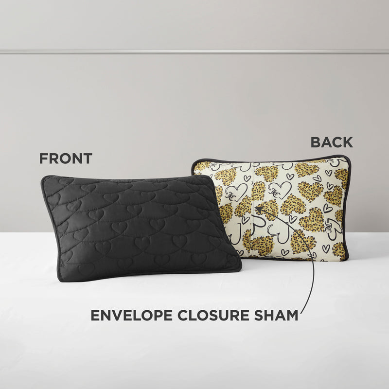 Two rectangular pillows are shown from the Cheetah Doodle Hearts Quilt Set: the front is black with a quilted heart pattern, while the back features a white and yellow leopard print with black trim. Labels show FRONT, BACK, envelope closure sham. Machine washable.