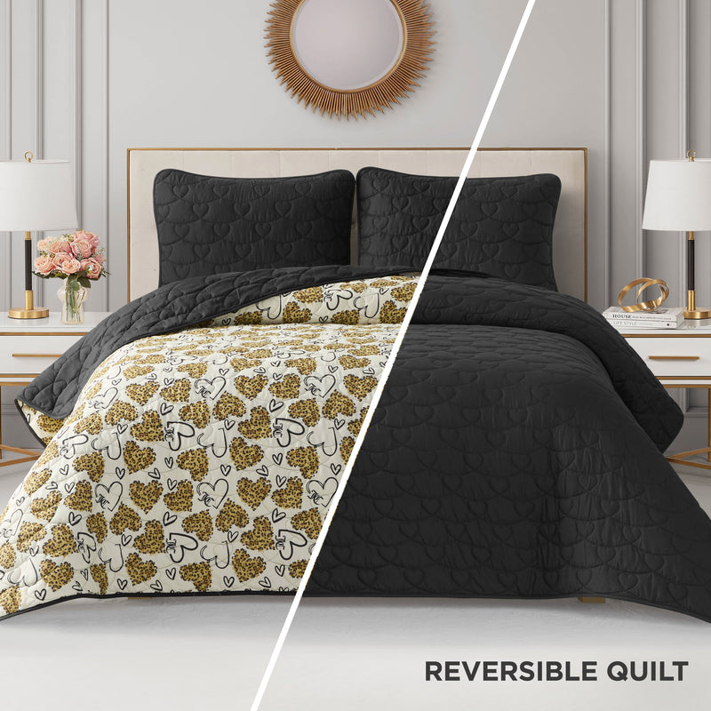 A split-image displays the Cheetah Doodle Hearts Quilt Set on a bed: one side is textured black, the other white with black and gold heart and floral patterns. This reversible, machine washable quilt set is styled in a modern room with gold accents.