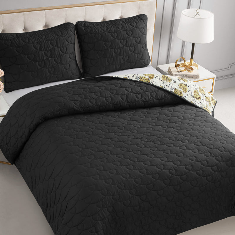 A neatly made bed features the reversible Cheetah Doodle Hearts Quilt Set with a quilted comforter, matching pillows, and a chic patterned underside. The bed has a beige upholstered headboard beside a white nightstand with lamp. Machine washable for easy care.