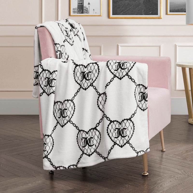 The Plush Oversized Throw Blanket with a black chain and heart pattern is draped over a pink armchair in a room with light walls and wooden floors, adding ultra-soft comfort and chic style to your space.