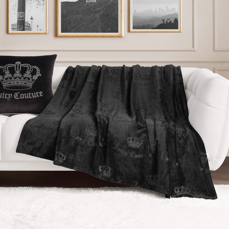 An Embossed Plush Oversized Throw Blanket is draped over a white sofa. In the background, a matching decorative pillow and framed wall art complete the cozy, coordinated look.