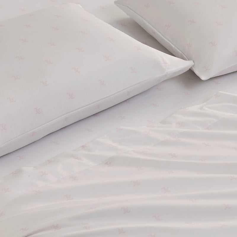 The Link Printed Bed in a Bag Bedding Set includes two white pillows and a neatly spread white bed sheet, all adorned with a light pink repeating logo pattern. The soft fabric ensures luxurious comfort and style for your bedroom.