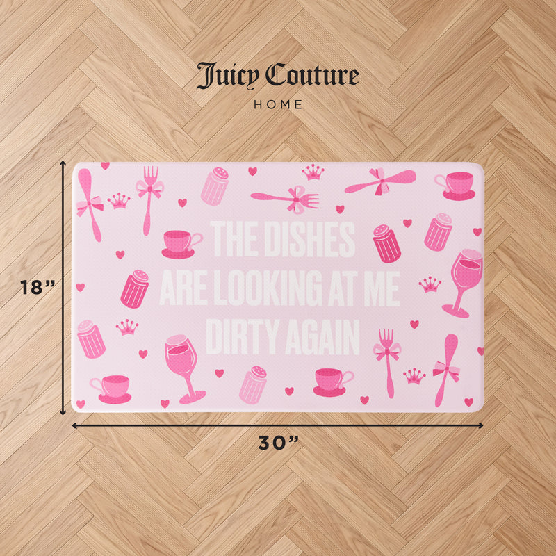 Introducing the Kitchen Wellness Mat in pink by Juicy Couture, decorated with whimsical kitchen-themed icons and the fun phrase: “THE DISHES ARE LOOKING AT ME DIRTY AGAIN.” Measuring 18 x 30 inches, this anti-fatigue mat brings both comfort and style to any kitchen floor, pictured here on a wood surface.