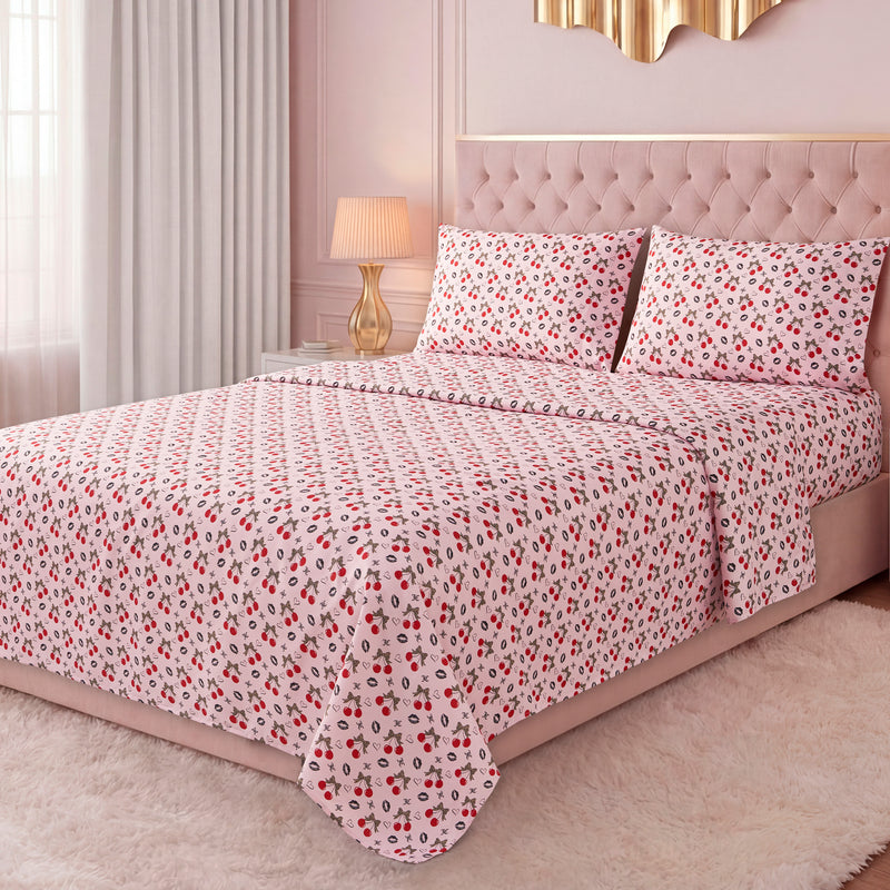 A bright bedroom features a neatly made bed with a pink tufted headboard, dressed in the Printed Microfiber Sheet Set with red and black floral patterns, complemented by pillows, curtains, a lamp, and a soft white rug.