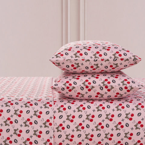 The Printed Microfiber Sheet Set includes two pillows and a sheet, all featuring red cherries, black and white bunnies, hearts, and white flowers on a soft pink background—a playful yet luxurious bedding choice.