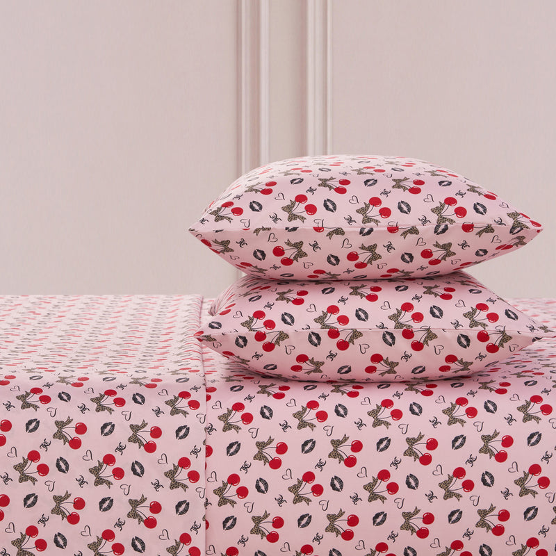 The Printed Microfiber Sheet Set includes two pillows and a sheet, all featuring red cherries, black and white bunnies, hearts, and white flowers on a soft pink background—a playful yet luxurious bedding choice.