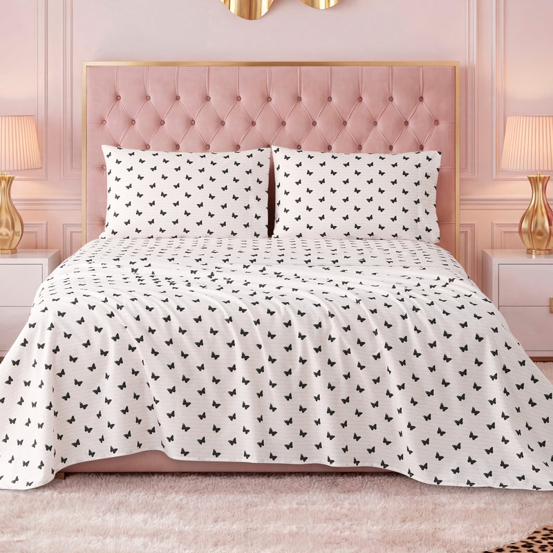 A neatly made bed with a pink tufted headboard and luxury bedding, including a white Printed Microfiber Sheet Set with a black butterfly pattern, flanked by white nightstands with lamps, in a pink-walled, elegant bedroom.