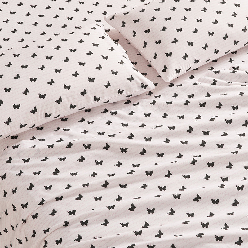A close-up of a bed with two pillows and a blanket, all covered in the Printed Microfiber Sheet Set featuring white fabric with a repeating pattern of small black butterflies.