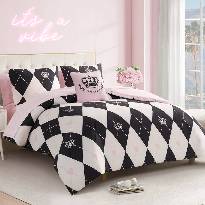 A stylish bedroom features the Royal Argyle Reversible Bed in a Bag Bedding Set with black and white argyle and crown motifs, pink accent pillows, pink walls, a neon "it's a vibe" sign, fresh flowers, and a window.