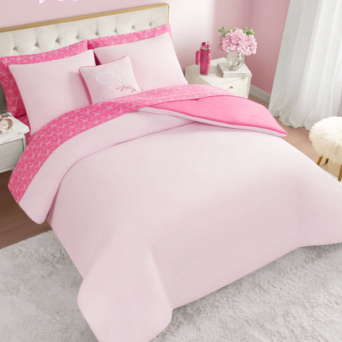 The Pearly Bows Reversible Bed in a Bag Bedding Set includes a pink bed, matching pillows, and a reversible comforter with bright pink patterned trim—perfect for a designer-inspired bedroom with light pink walls, white furniture, flowers, and a soft rug.