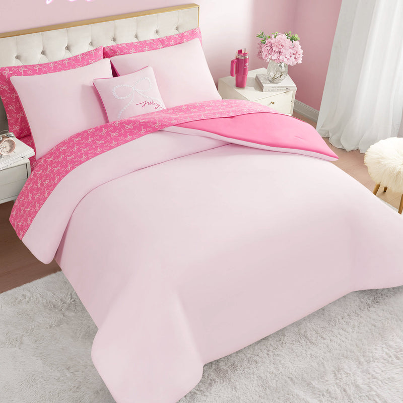 The Pearly Bows Reversible Bed in a Bag Bedding Set includes a pink bed, matching pillows, and a reversible comforter with bright pink patterned trim—perfect for a designer-inspired bedroom with light pink walls, white furniture, flowers, and a soft rug.