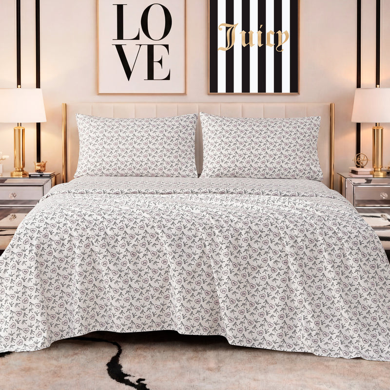 A neatly made bed features the Printed Microfiber Sheet Set in white and gray, flanked by mirrored nightstands and gold lamps. Behind the bed, two framed prints—one reading LOVE, the other Juicy—complete the luxurious look.