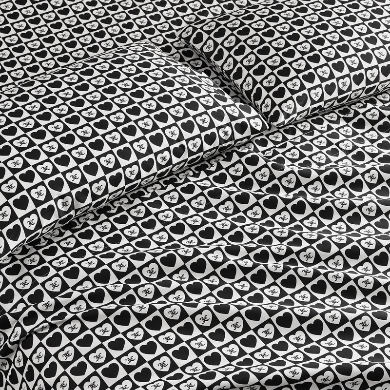 The Printed Microfiber Sheet Set features a bold black-and-white design with hearts and “NYC” text, creating a stylish look on the pillowcases and comforter—ideal for anyone who loves luxury bedding.