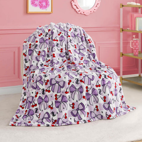 A Kids Plush Throw Blanket featuring purple bows, red cherries, and black anchors is draped over a chair in a pink room decorated with elegant accents and wall art.