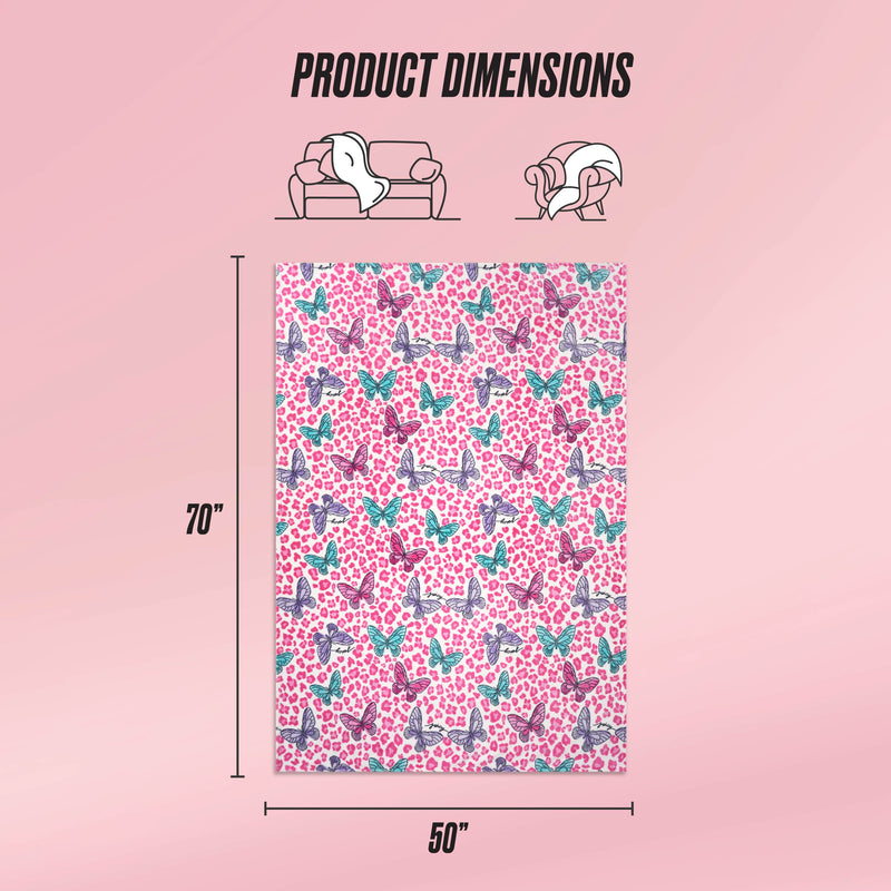 The Kids Plush Throw Blanket by Juicy Couture comes in pink with playful butterfly and heart designs. Measuring 70" x 50", it’s ultra-soft, perfect for kids, as shown draped over a sofa and person. Text displays: Product Dimensions.