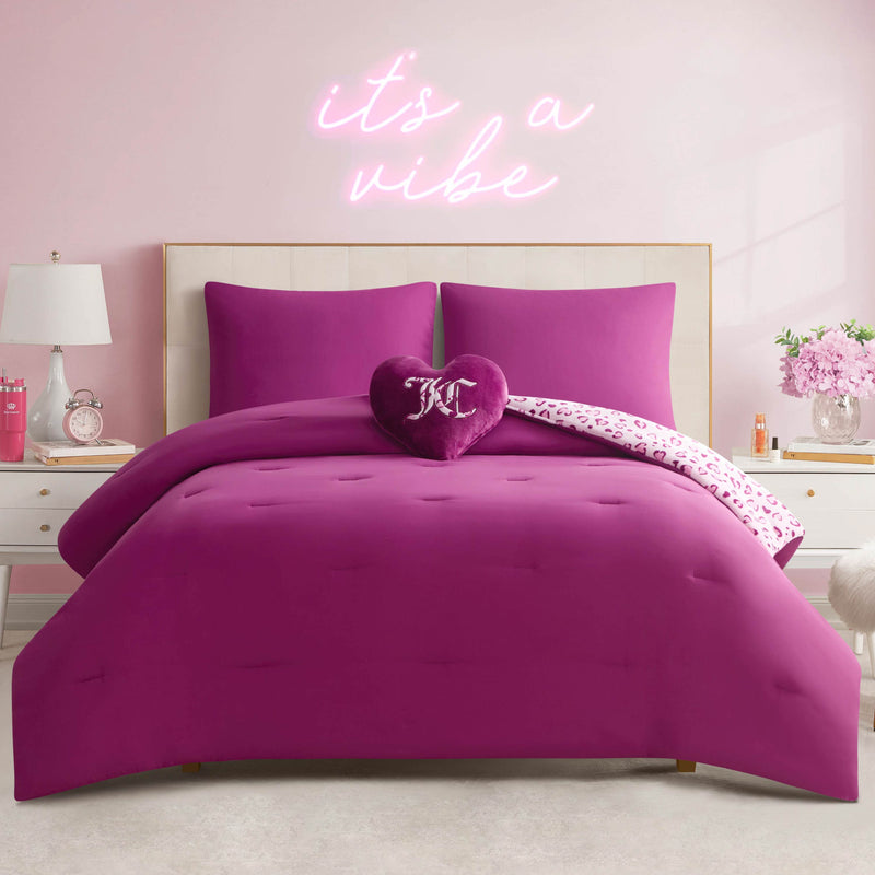 A neatly made bed with the Plush Reversible Leopard Hearts Comforter Set and a decorative pillow sits against a light pink wall with a neon “it’s a vibe” sign above. White nightstands, lamps, and pink accents add extra flair to the room.