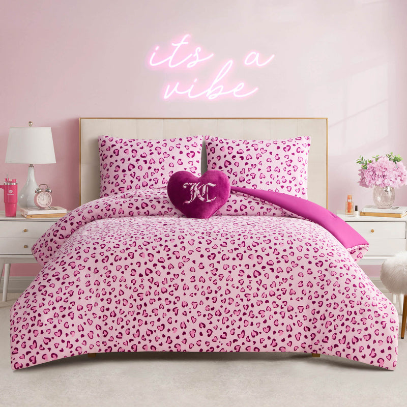A pink bedroom featuring the Plush Reversible Leopard Hearts Comforter Set, matching decorative pillows, a heart-shaped pillow, and an “it’s a vibe” neon sign above the bed. White nightstands and pink accents complete the chic look.