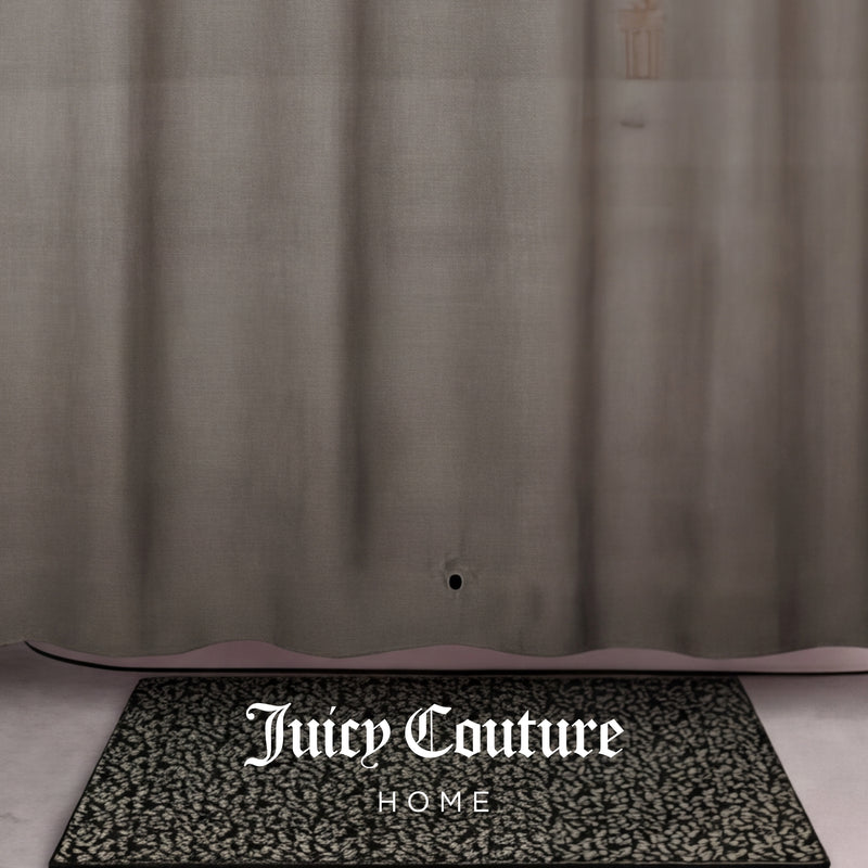 A patterned black and white doormat with Juicy Couture HOME sits in front of a sheer tan PEVA Shower Curtain Liner, which has a small hole near the bottom.