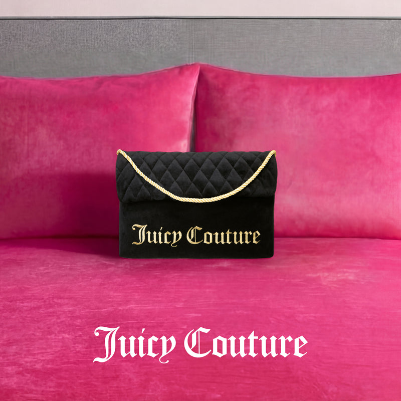 A Purse Decorative Pillow inspired by Juicy Couture, featuring black fabric with gold lettering and a gold rope handle, sits on a bright pink velvet bed accented with matching trendy pillows. The Juicy Couture logo appears in white on the bed.