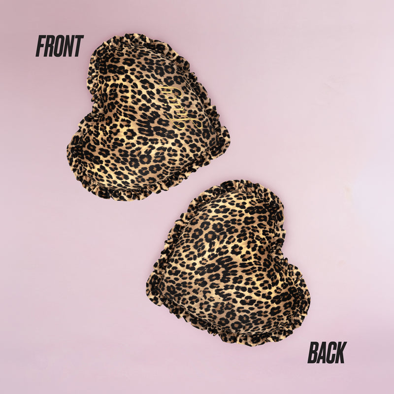 The Heart Shaped Decorative Pillow features a chic Juicy Couture-inspired cheetah print, shown front and back on a light pink background, with both sides displaying the same stylish pattern.